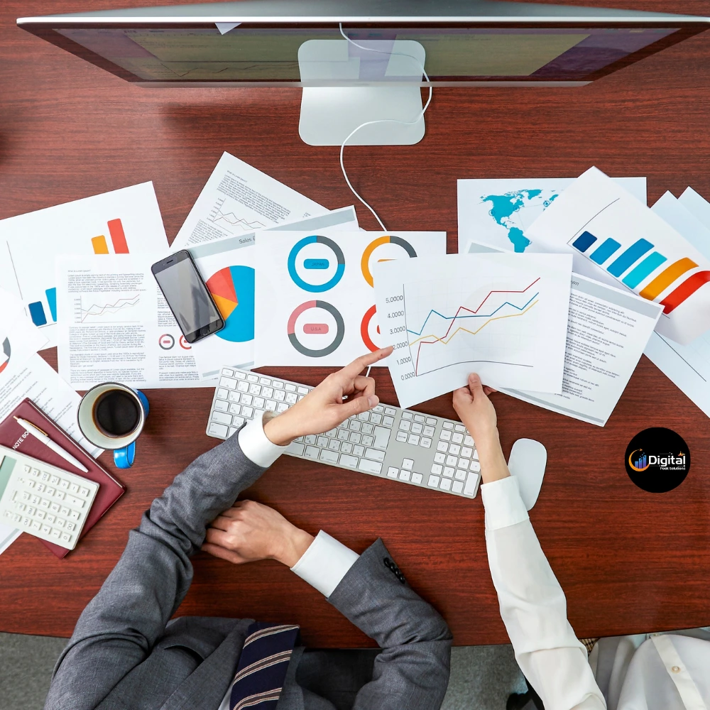 verhead view of two people collaborating on a desk with charts and graphs, representing marketing analysis.